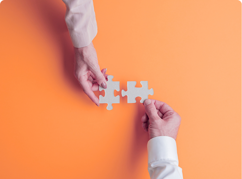 Two hands bringing together the last two pieces of a jigsaw puzzle against an orange background
