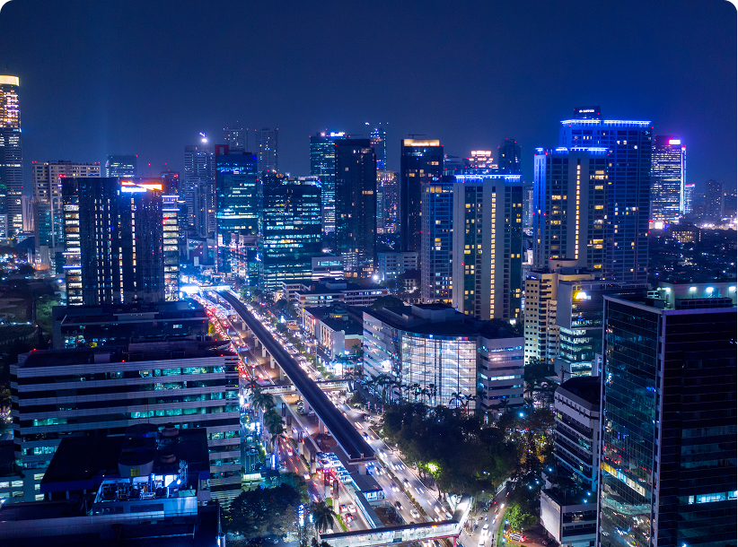 A city skyline of lit office and residential towers above a busy road at night