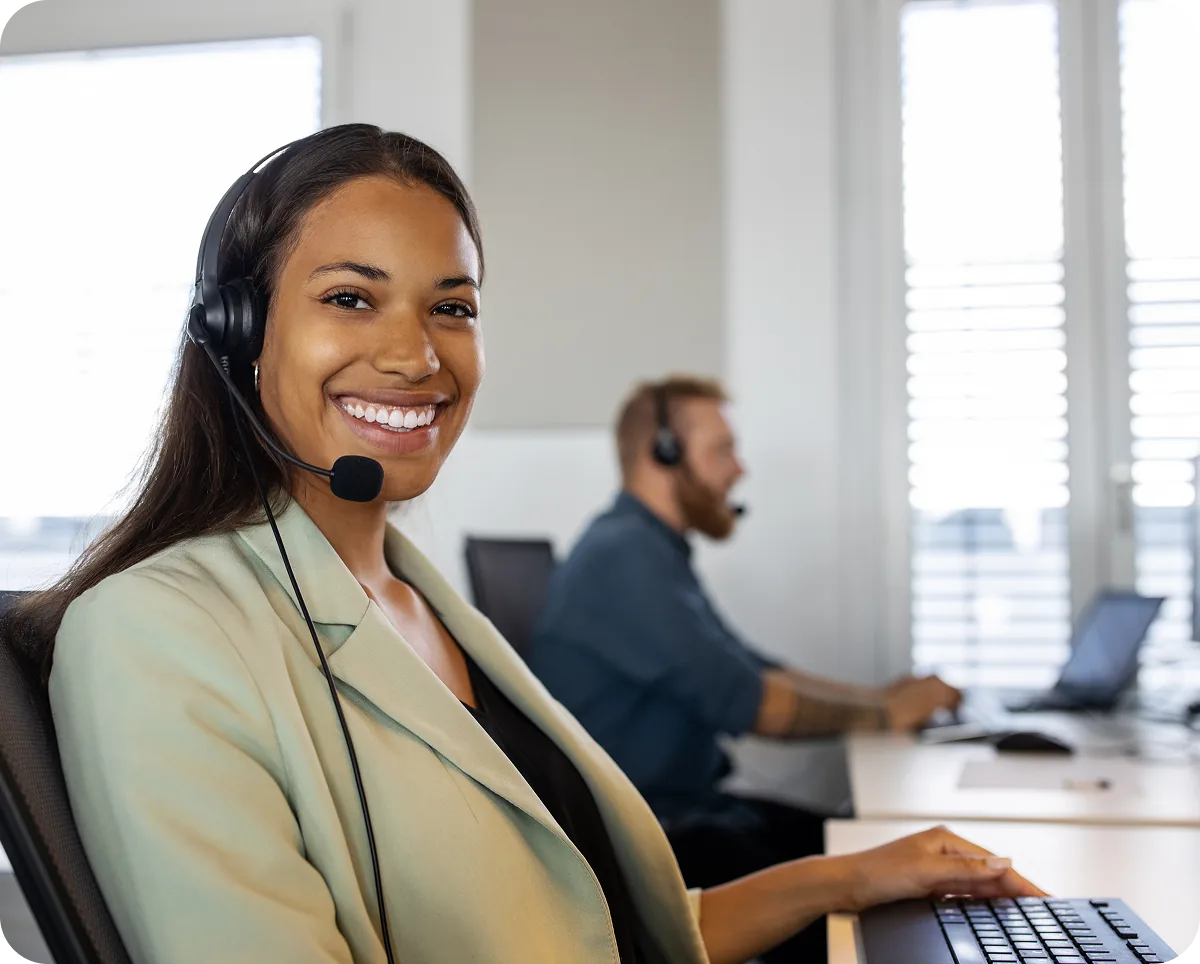 A smiling support agent wearing a headset at her desk