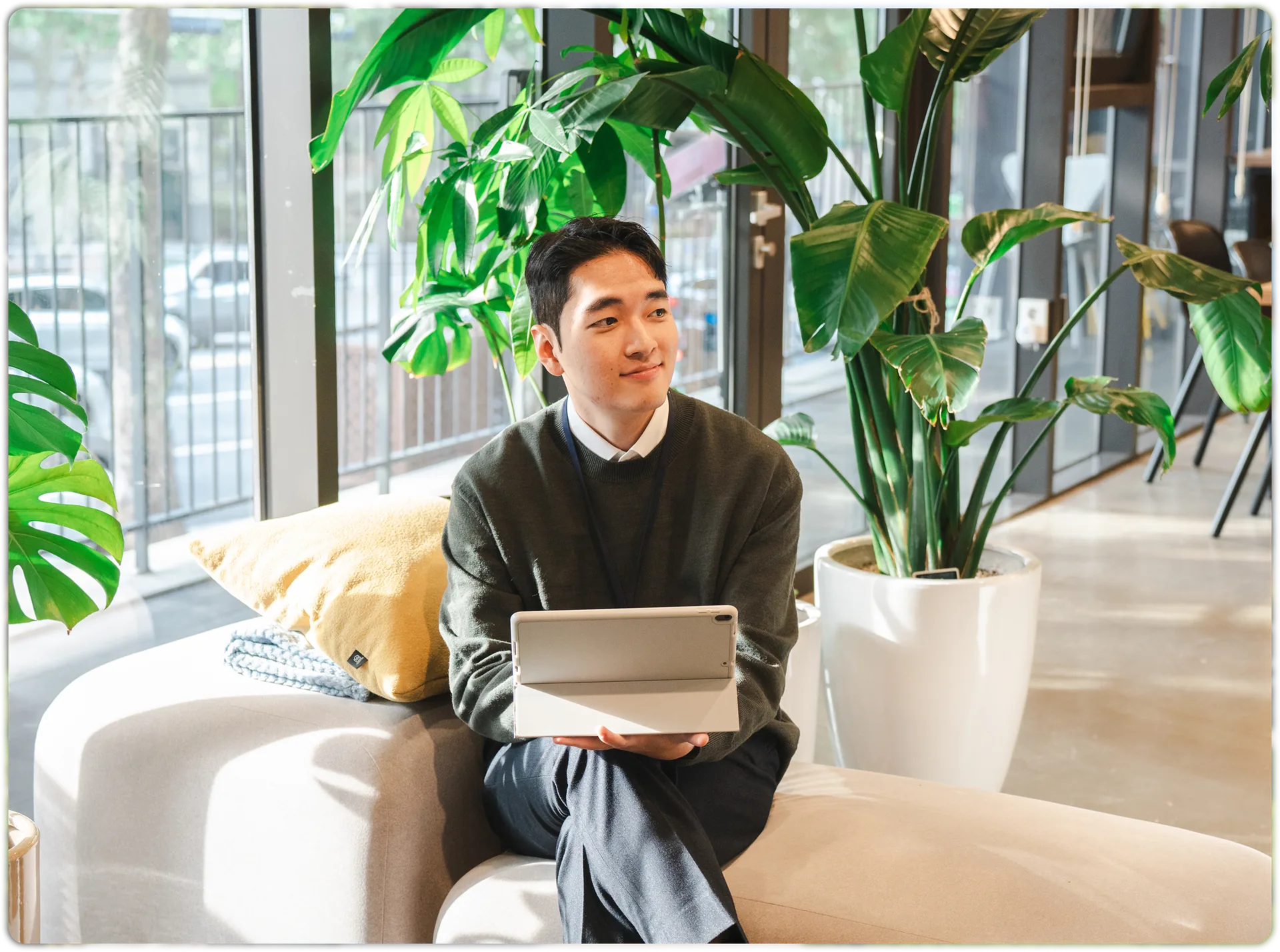 A resident sitting with a tablet in a plant-filled lounge