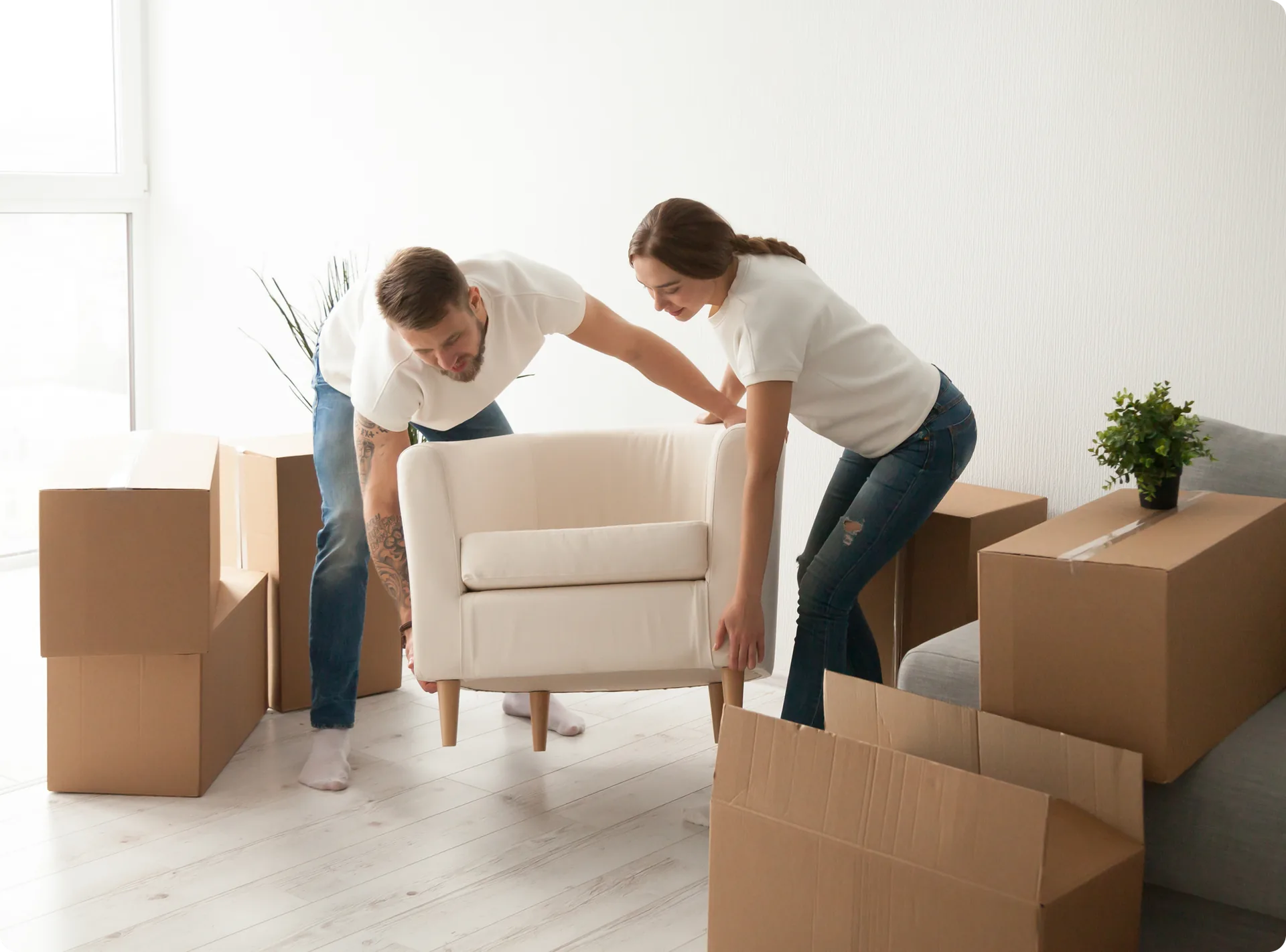 A couple carrying an armchair between moving boxes