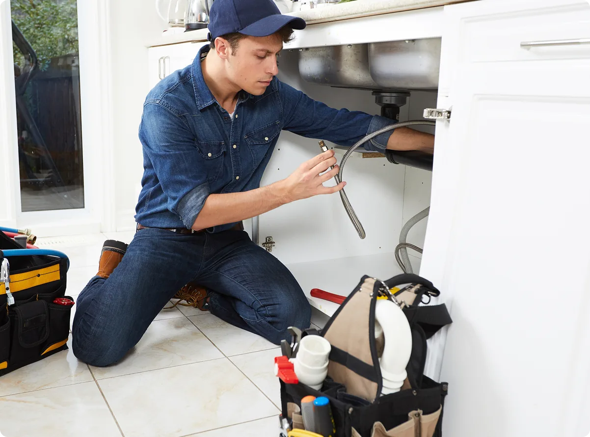 A plumber working on a pipe beneath a kitchen sink
