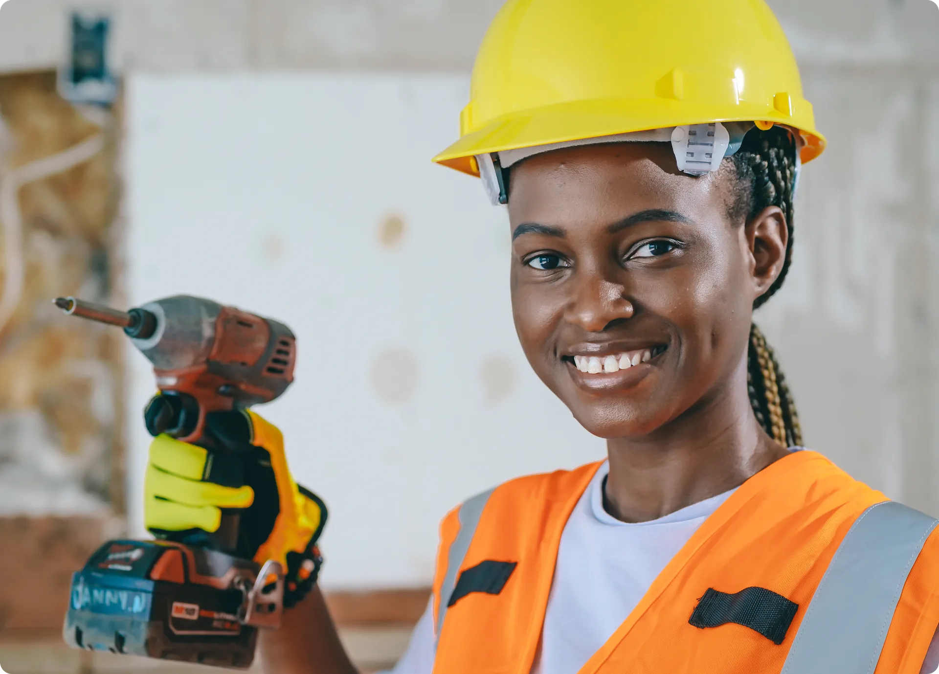 A tradesperson in a hard hat and safety vest holding a power drill